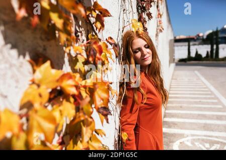 Junge Frau in rotem Kleid mit geschlossenen Augen gegen stehen ivy Wall Stockfoto