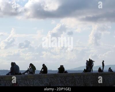 Silhouetten von Menschen chillen auf einem Kai an einem hellen Dezembertag, Alimos, Griechenland Stockfoto