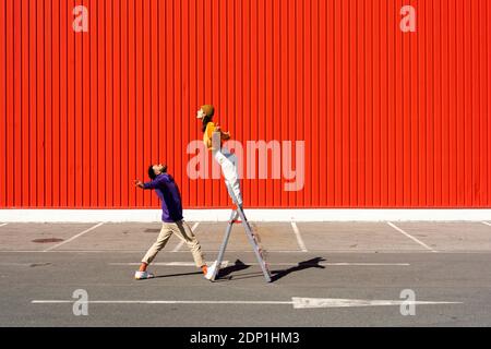 Junge Männer und Frauen, die mit einer Leiter vor sich auftreten Einer roten Wand Stockfoto