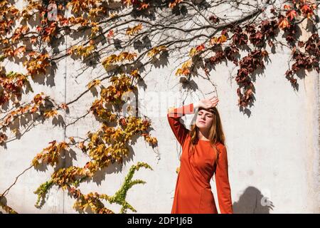Frau mit der Hand auf dem Kopf, die gegen die Efeu-Wand steht Stockfoto