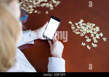 Alte Frau mit Blick auf Smartphone, während Sie ein Puzzle Stockfoto