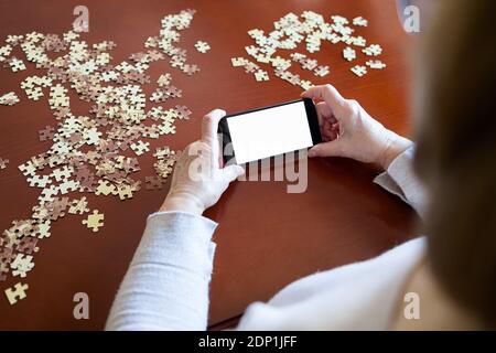 Alte Frau mit Blick auf Smartphone, während Sie ein Puzzle Stockfoto