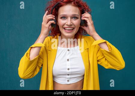 Junge Frau mit roten lockigen Haaren trägt Kopfhörer Spaß haben Musik hören Stockfoto