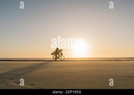 Surfer auf einem Fahrrad während des Sonnenuntergangs in der Strand Costa Nova, Portugal Stockfoto