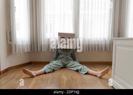 Frau trägt einen Karton auf dem Kopf mit gelangweilten Smiley sitzen Auf dem Boden Stockfoto