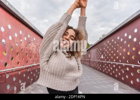 Lächelnde Frau streckt die Hand, während sie auf der Brücke gegen den Himmel steht Stockfoto