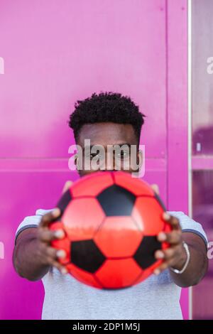 Nahaufnahme eines jungen Mannes, der den Fußball gegen die rosa Farbe hält Stockfoto