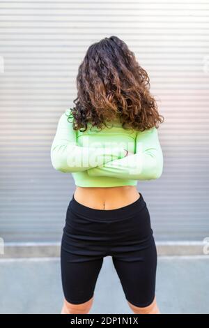 Junge Frau trägt grüne Crop Top mit Haaren vorne Von Gesicht posiert gegen graue Wand Stockfoto