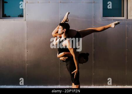 Professionelle männliche Turnerin hält Frau auf dem Kopf während des Tanzes Haltung an der Wand Stockfoto