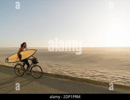 Surfer auf einem Fahrrad während des Sonnenuntergangs in der Strand Costa Nova, Portugal Stockfoto