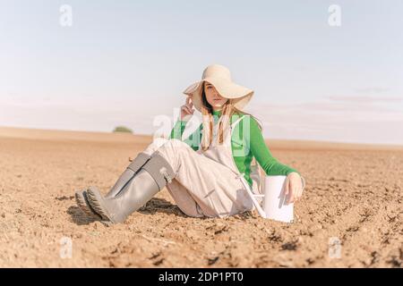 Junge Frau mit Gießkanne auf trockenem Feld sitzen Stockfoto