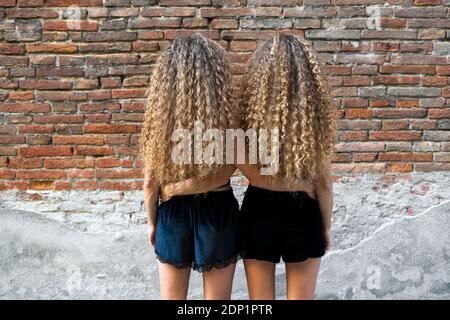 Rückansicht des Twin sisters mit korkenzieherlocken ständigen Arm in Arm Seite an Seite Stockfoto