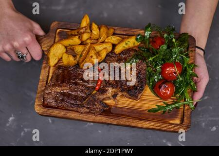 Rindersteak mit scharfem Chili auf einem Holzbrett mit Kartoffelscheiben. Stockfoto