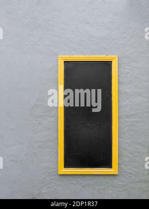 Tafel, schwarze Tafel an Außenwand für Menü etc. Montiert Alter Hintergrund. Gelber Rahmen. Stockfoto