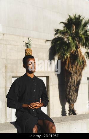 Junger Mann mit schwarzem Kaftan, der eine Ananas auf dem Kopf balanciert Stockfoto