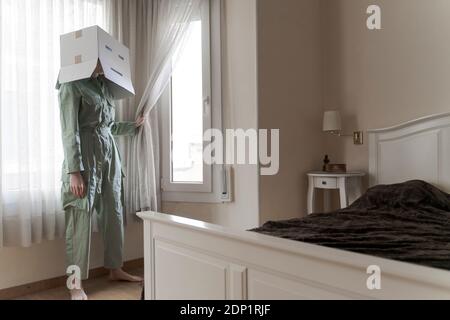 Frau trägt einen Karton auf dem Kopf mit gelangweilten Smiley suchen Aus dem Fenster Stockfoto