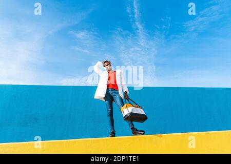 Junge trendige Mann stand auf gelbe Wand, Musik hören Stockfoto