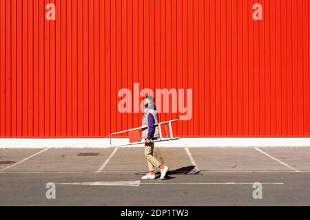 Junger Mann, der eine Leiter vor einem roten trägt Wand Stockfoto