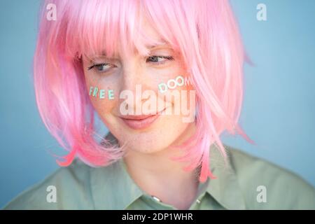 Junge Frau trägt rosa Perücke, Buchstaben auf ihrem Gesicht, freies Doom Stockfoto