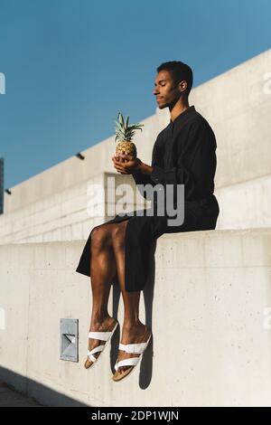 Junger Mann mit schwarzem Kaftan, der eine Ananas hält Stockfoto