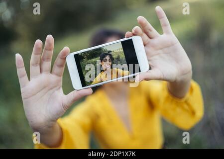 Glückliche junge Frau tragen gelbe Kleid mit einem weissen Smartphone vor ihrem Gesicht und das Nehmen eines selfie Stockfoto