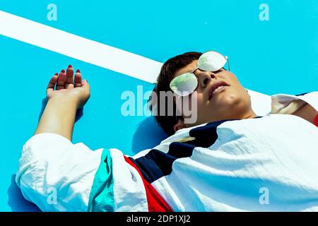 Porträt einer Frau, die eine Spiegelsonnenbrille trägt und auf dem Boden liegt Stockfoto