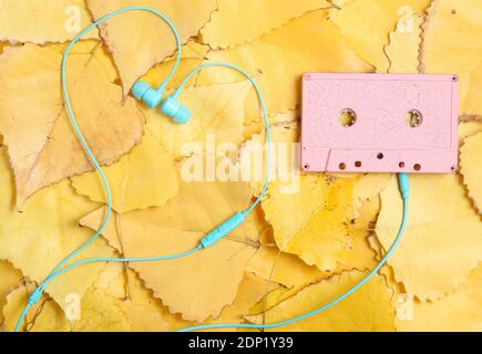 Audiokassette und Kopfhörer auf gelb gestürzten Blättern. Draufsicht. Retro-Technologie. Herbstzeit Stockfoto