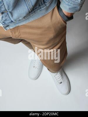 Fragment der männlichen Beine in beigen Hosen und weißen Sneakers steht auf weißem Hintergrund. Draufsicht. Stockfoto
