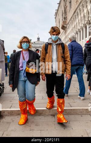 Besucher, die wasserfeste Plastikschuhebezüge in der Nähe des Markusplatzes während der Acqua Alta (hohe Flut), Venedig, Italien tragen. Stockfoto