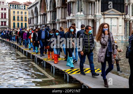 Tourists Walking On A Raised Platform During Acqua Alta (High Tide) St Mark’s Square, Venice, Italy. Stock Photo