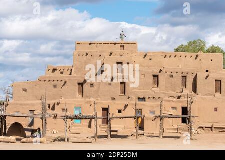 Mann reinigt das Dach von lehmziegelhäusern im historischen indianischen Dorf Taos Pueblo, New Mexico, USA. Ein UNESCO-Weltkulturerbe. Stockfoto