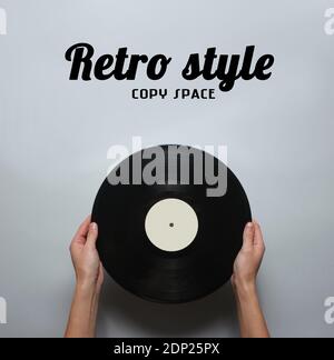 Weibliche Hände mit einer Retro-Vinyl-Platte auf einem grauen Hintergrund. Aussicht von oben, minimalistisch. Stockfoto
