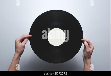 Weibliche Hände mit einer Retro-Vinyl-Platte auf einem grauen Hintergrund. Aussicht von oben, minimalistisch. Stockfoto