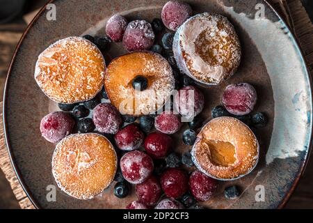 Gefrorene Beeren, Pflaumen und Kirschen auf einem braunen Teller auf einem Holzhintergrund. Stockfoto