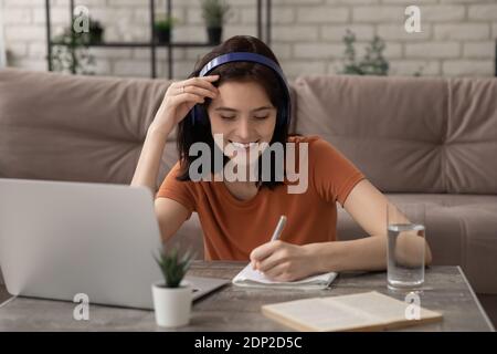 Konzentrierte Frau Student Handschrift Essay in Kopfhörer von pc gesetzt Stockfoto