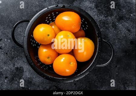 Gelbe Kirschtomaten in einem Sieb. Schwarzer Hintergrund. Draufsicht. Stockfoto