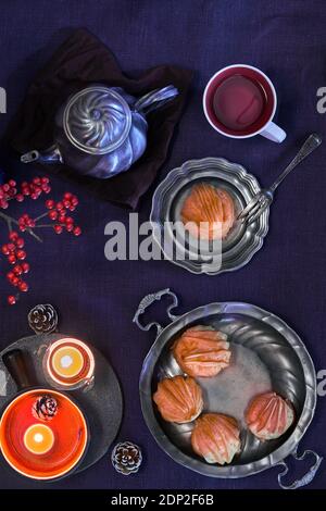 Leckere Eclare oder Braukuchen und Zinn Teekanne und Tasse Tee. Natürliches Weihnachtsdekor, Kerzen, rote Beeren. Weihnachten flach lag auf dunkelviolett Stockfoto