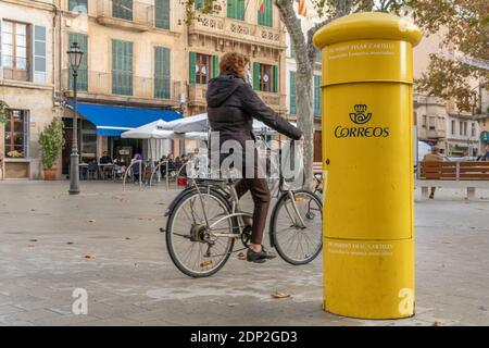 Llucmajor, Spanien; dezember 17 2020: Gelbe Briefkasten der spanischen Post. Im Hintergrund das Bild eines Quadrats mit einer Frau, die auf einem Bicycl reitet Stockfoto