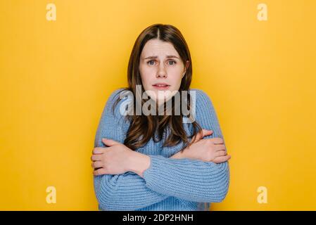 Junge Brünette Frau friert in der leichten Kleidung erwärmt sich durch Umarmung sich, saisonale Veränderungen niedrige Temperatur Heizungsproblem, Schüttelfrost Gefühl von Coldne Stockfoto