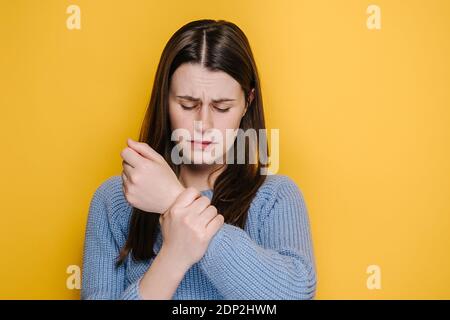 Müde ungesunde junge Frau massieren schmerzhafte Hand, leiden Karpaltunnelsyndrom, in blauen Pullover gekleidet, Modelle über gelben Studio-Hintergrund. Stockfoto