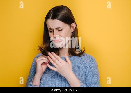 Traurige junge Frau, die auf Spliss schaut, isoliert auf gelbem Studiohintergrund. Weibliche Hormonprobleme oder Vitaminmangel. Unglückliches Mädchen fühlt sich aufgeregt ein Stockfoto