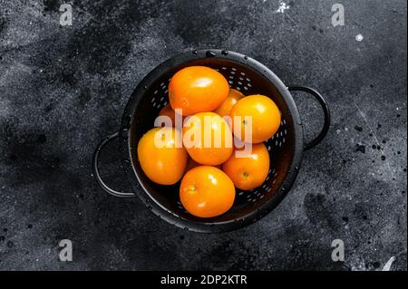 Rohe frische gelbe Tomaten in einem Sieb. Schwarzer Hintergrund. Draufsicht. Stockfoto