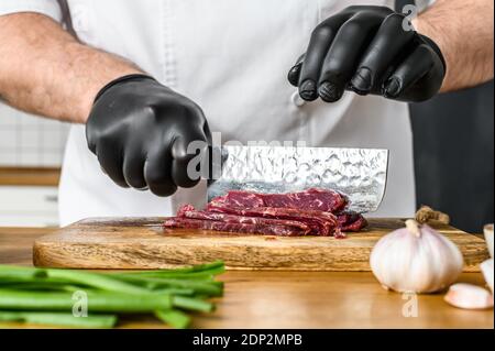 Mann schneidet rohes Rindfleisch Fleisch. Ein Koch in schwarzen Handschuhen. Konzept des Kochens von Rindfleisch Tartare. Stockfoto