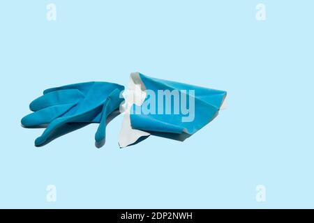 Abgenutzter, zerrissener blauer Medizinhandschuh auf hellblauem Hintergrund. Gesundheitsfachkräfte arbeiten unter sehr schwierigen Bedingungen. Stockfoto