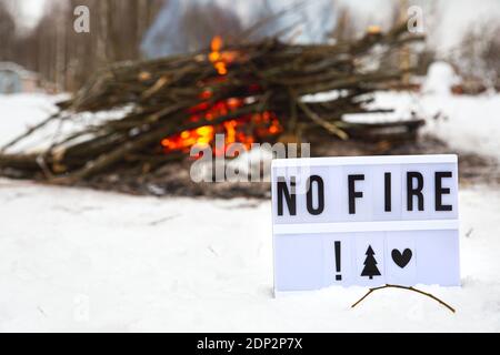 Ein Schild mit dem Text kein Feuer vor dem Hintergrund eines großen lodernden Feuers. Das Konzept des Naturschutzes, Schutz vor Waldbränden, Ökologie. Stockfoto