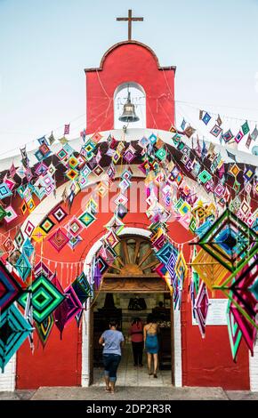 Menschen, die die Hauptkirche in Sayulita, Nayarit, Mexiko betreten, sind außen mit Ojo de Dios oder "Gottes Auge" geschmückt, einem lokalen Symbol und Handwerk der Indige Stockfoto