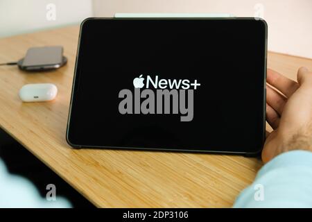 Apple News plus Logo auf dem Bildschirm des iPad Tablet Mit Smartphone iPhone Aufladen auf dem kabellosen Ladegerät und airpods im Gehäuse auf dem Hintergrund Stockfoto