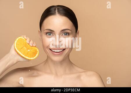 Frau mit perfekter Gesichtshaut, gekämmte Haare, quetschen orange. Lächelndes Weibchen mit natürlichem Make-up und Zitrusfrüchten auf beigem Hintergrund. Vitamin C, beaut Stockfoto