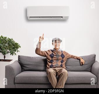 Älterer Mann auf einem Sofa sitzend, der auf eine zeigt Klimaanlage an der Wand Stockfoto