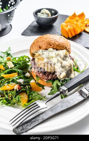 Burger mit Blauschimmelkäse, marmorierte Rind- und Zwiebelmarmelade, eine Beilage Salat mit Rucola und Orangen. Weißer Hintergrund. Draufsicht. Stockfoto